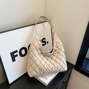 Chic quilted beige shoulder bag with puffy texture and integrated wide strap on a shelf