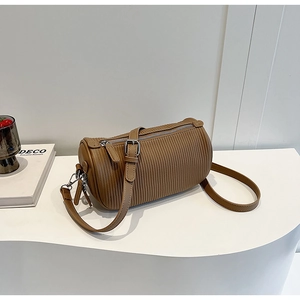 Detail of coffee brown pleated cylinder crossbody bag with adjustable strap on white pedestal