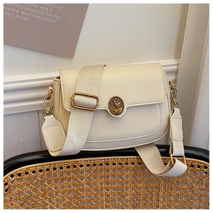 Detail of a creamy white saddle bag featuring a vintage gold medallion and wide strap
