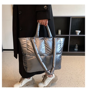 Silver quilted down tote bag styled with black coat in a minimalist interior setting