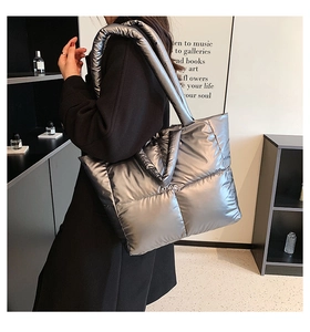 Close-up of a silver quilted puffer tote bag worn by a model in a modern interior