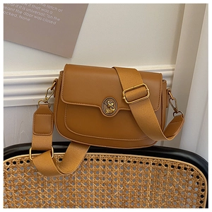 Close-up of brown matte leather saddle bag with vintage metal logo and woven strap