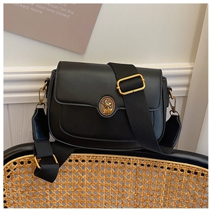 Detail of vintage black crossbody bag with gold crest on a rustic rattan chair