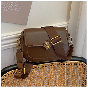 Detail of vintage brown leather bag with golden emblem on a woven chair