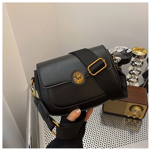 Detail of black crossbody bag featuring a golden relief buckle and wide fabric strap