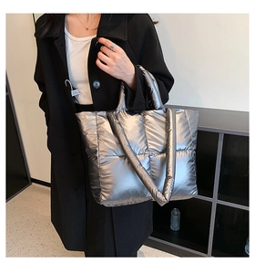 Silver quilted tote bag in metallic finish worn over a black winter coat as a shoulder bag