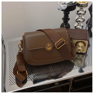 Close-up of vintage brown leather crossbody bag with embossed metal emblem and wide strap