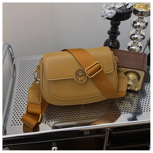 Close-up of brown saddle bag featuring vintage gold emblem and wide woven strap