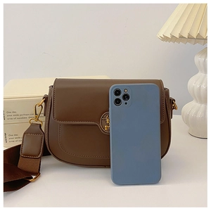 Brown semi-circle crossbody bag shown next to a smartphone for size reference