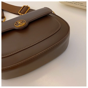 Detail of dark brown leather crossbody bag with vintage gold emblem and canvas strap