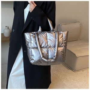 Silver quilted down tote bag with metallic finish shown on shoulder in a minimalist room