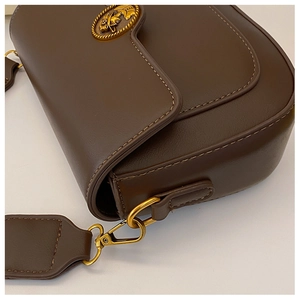 Detail of vintage dark brown leather saddle bag with ornate gold metal buckle clasp