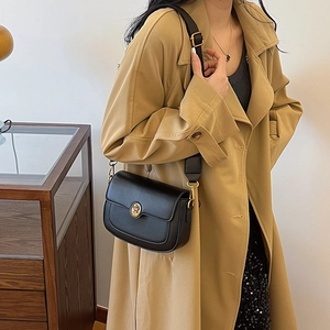 Minimalist black leather crossbody bag with vintage gold emblem worn by a model