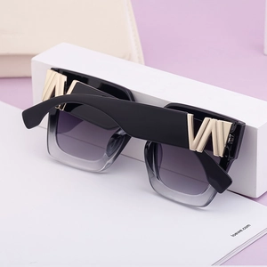 Detail of square black sunglasses with wide temples and gold geometric metal hardware
