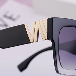 Macro shot of gold V-shaped hinge detail and gradient lens on square sunglasses