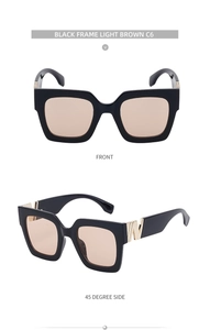 Detail of square black frame sunglasses with light brown lenses and gold hinge accents