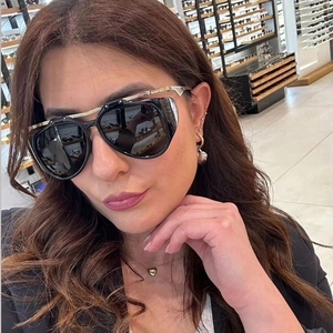 Detail of oversized black pilot sunglasses with gold metal top bar worn by a model