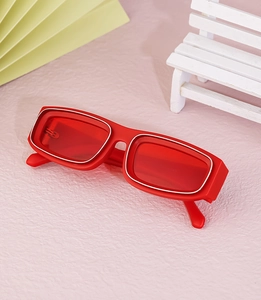 Detail view of red rectangular sunglasses with silver metal trim on a stylish pink surface