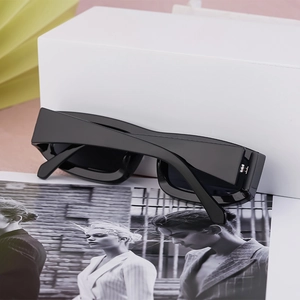Detail of square black sunglasses resting on a white box over a fashion magazine