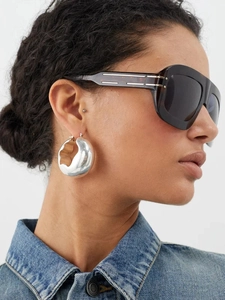 Close-up of polished silver chunky hoop earrings worn by a model with sunglasses