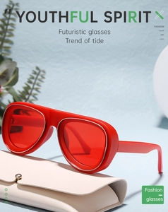Gros plan de lunettes aviateur rouges futuristes sur un étui en cuir beige et fond végétal