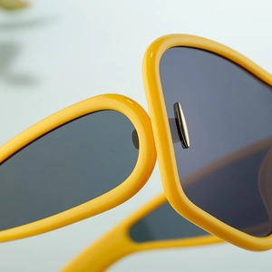Close-up of bright yellow sunglasses frame with gold metal trim and dark grey lenses