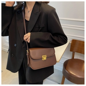 Brown leather crossbody bag detail featuring a polished gold rectangular metal buckle