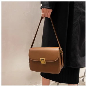 Detail of a brown leather shoulder bag with a gold buckle worn with a black coat