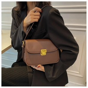 Close-up of brown vintage rectangle crossbody bag with gold buckle on black blazer