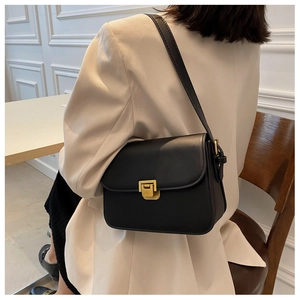 Detail of a vintage black leather crossbody bag with gold buckle on a model