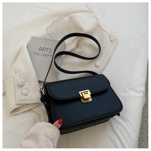 Close-up of black crossbody bag with gold square buckle on textured white fabric