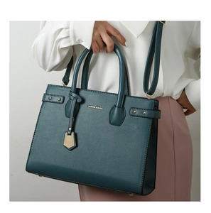 Dettaglio della borsa tote verde scuro con trama litchi e ciondolo metallico
