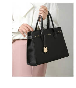 Dettaglio di una borsa tote in pelle nera con trama litchi e rifiniture dorate