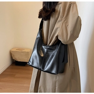 Détail de la texture d'un grand sac hobo noir avec large bandoulière sur le modèle