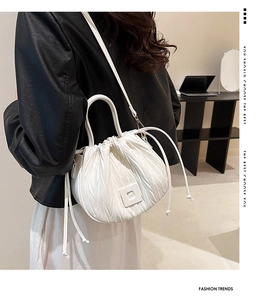 Detail view of a white pleated drawstring bucket bag styled with a black leather jacket