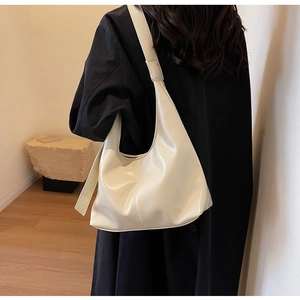 Sac hobo chic blanc cassé en similicuir plissé porté sur un élégant manteau noir
