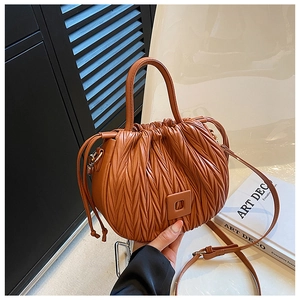Detail of caramel pleated bucket bag showing drawstring closure and adjustable strap