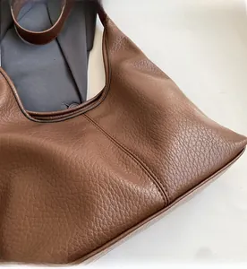 Detail of brown hobo bucket bag with pebbled leather texture and reinforced black edges