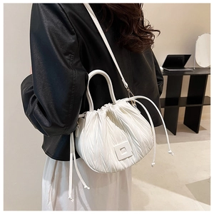 Detail of white pleated bucket bag with drawstring closure and slim shoulder strap