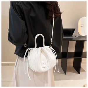 Detail of white pleated drawstring bucket bag with rigid handle and detachable strap