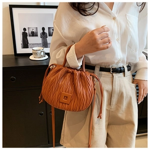 Close-up of a brown orange pleated bucket bag with drawstring and curved handle