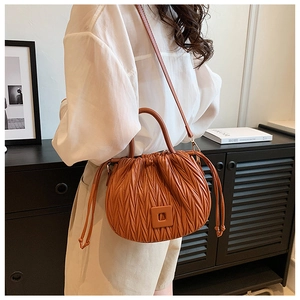 Brown pleated drawstring bucket bag shown on model in a modern minimalist interior room