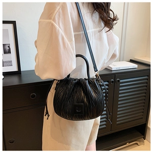 Detail of black pleated crossbody bag with drawstring closure and metal buckle on model