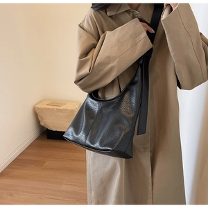 Detailed side view of black lychee grain leather bucket bag worn with a khaki trench coat