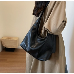 Detail shot of a black hobo bag with pebble texture styled with a beige trench coat