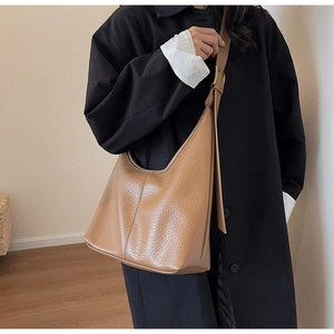 Detail of tan lychee pattern shoulder bag featuring wide strap and metal buckle on model