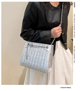 Detail of silver pleated crossbody bag with chain strap worn by a model in black leather jacket