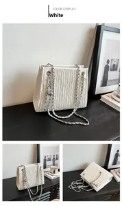 Close-up of white quilted tote bag with silver chain strap and metal ball charm detail