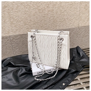 Close-up detail of white pleated shoulder bag with silver metal chain straps