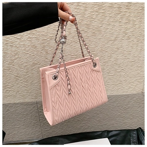 Detail of light pink quilted handbag with silver chain straps and V-shaped texture